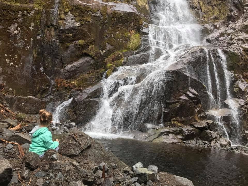 A little girl in a turquoise jacket looking at a waterfall.