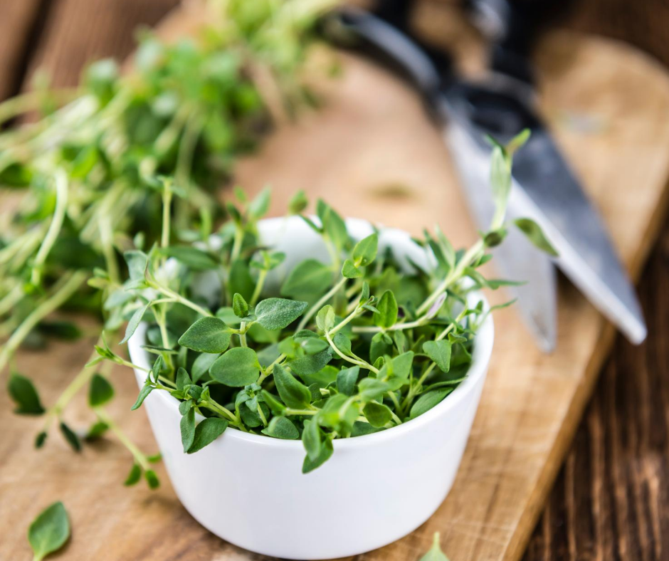 A white bowl filled with herbs on a wooden chopping board with black scissors.