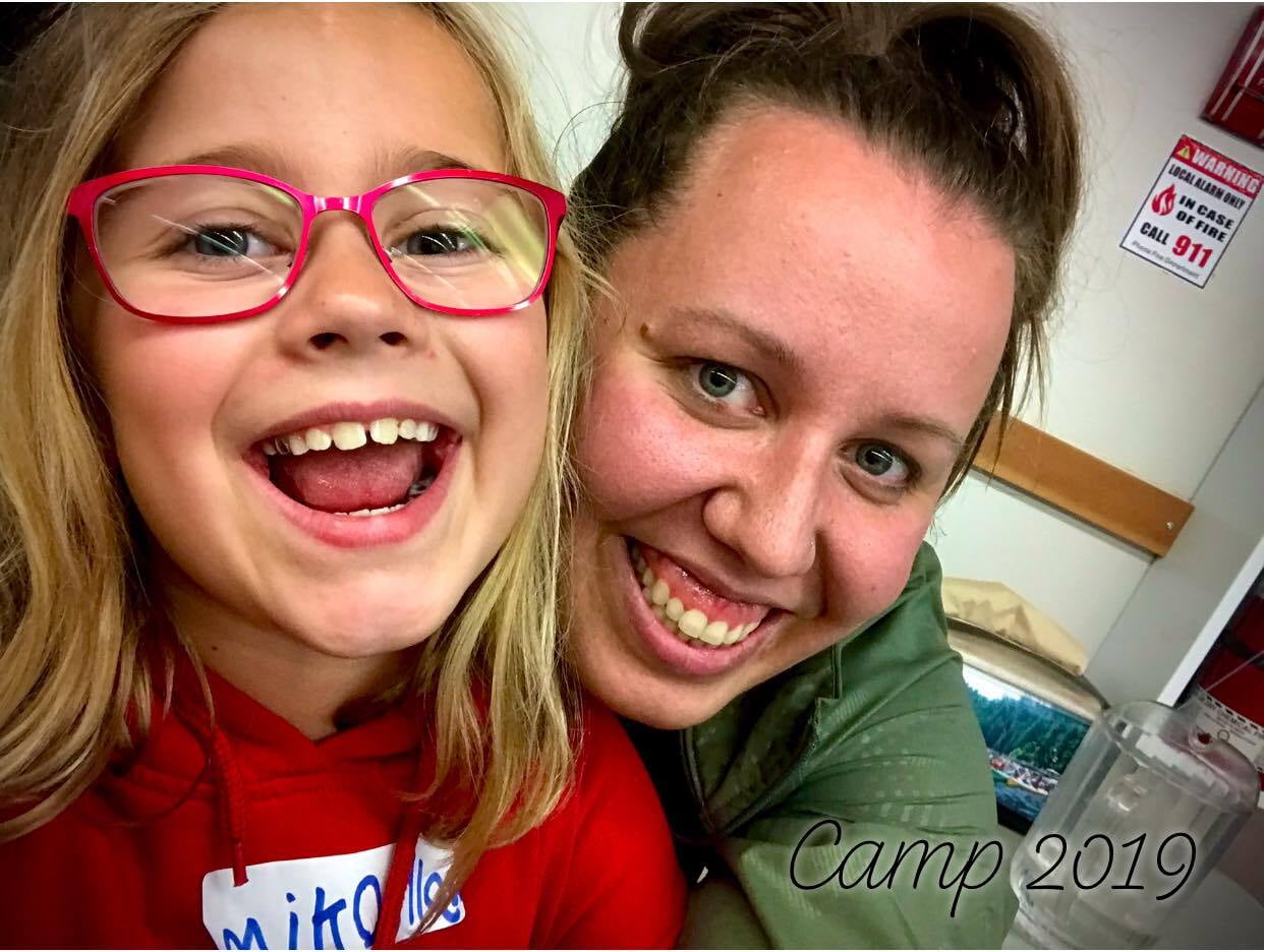 A little girl with pink glasses in a red hoody and a women smiling next to her wearing a green jacket.