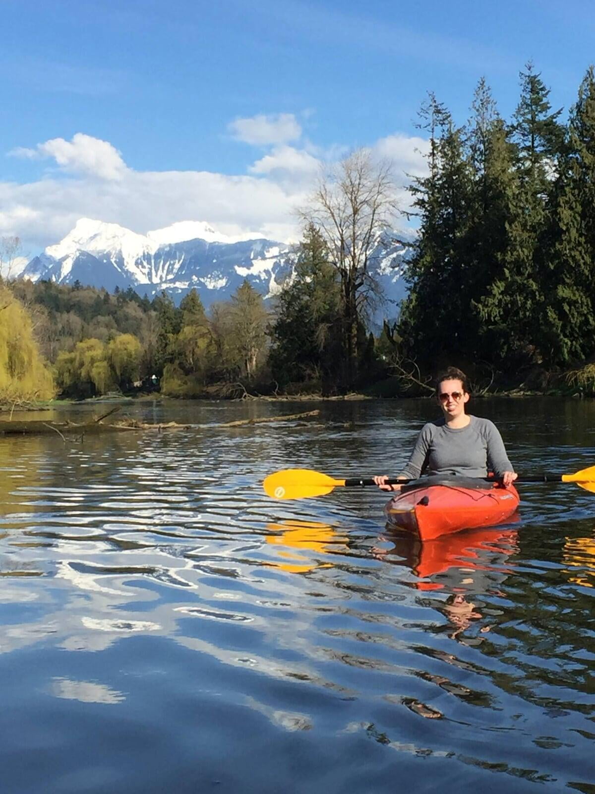 A women in the water in a kayak with paddles in hand smiling.