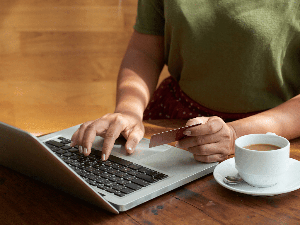 A man on his laptop with a credit card in hand and a white mug filled with coffee next to it.