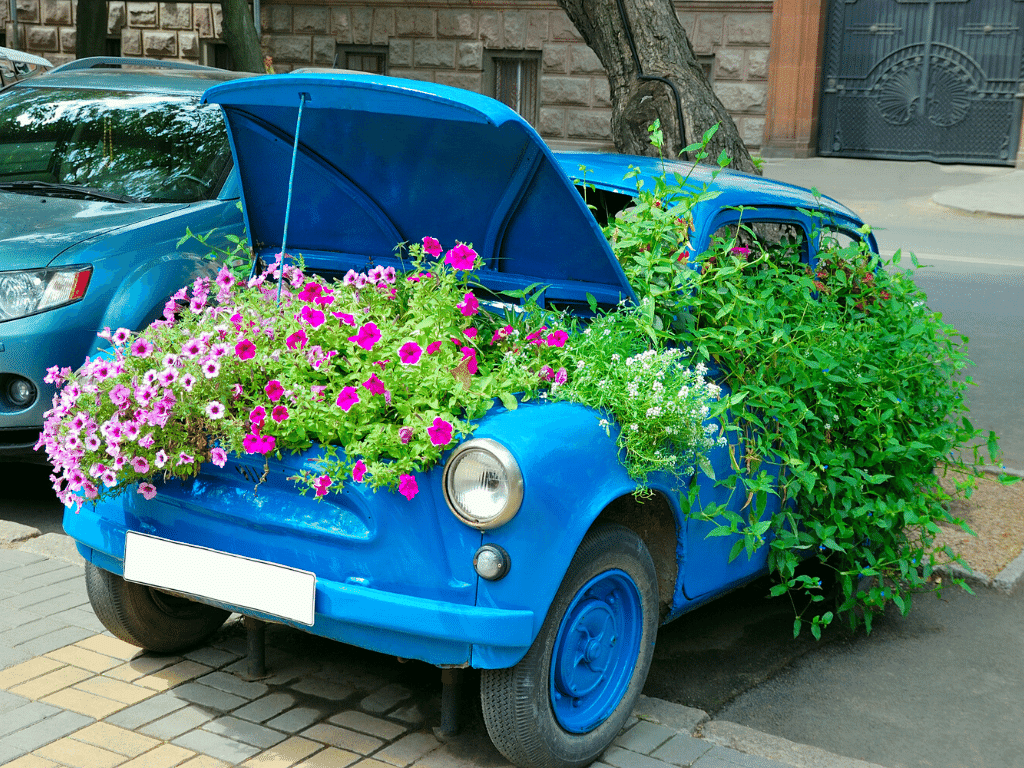 A blue car that is completely filled with flowers with the hood open filled with more flowers.